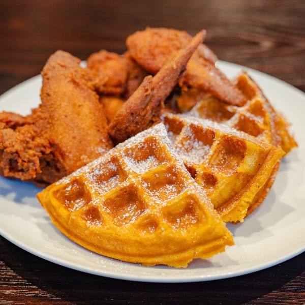 Crispy fried chicken pieces and golden waffles dusted with powdered sugar on a white plate.