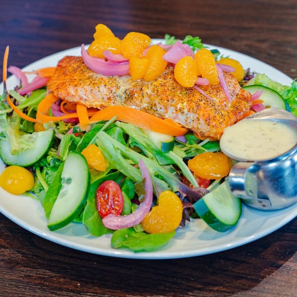 Salmon fillet salad with mixed greens, mandarin oranges, pickled onions, cucumbers, and dressing.