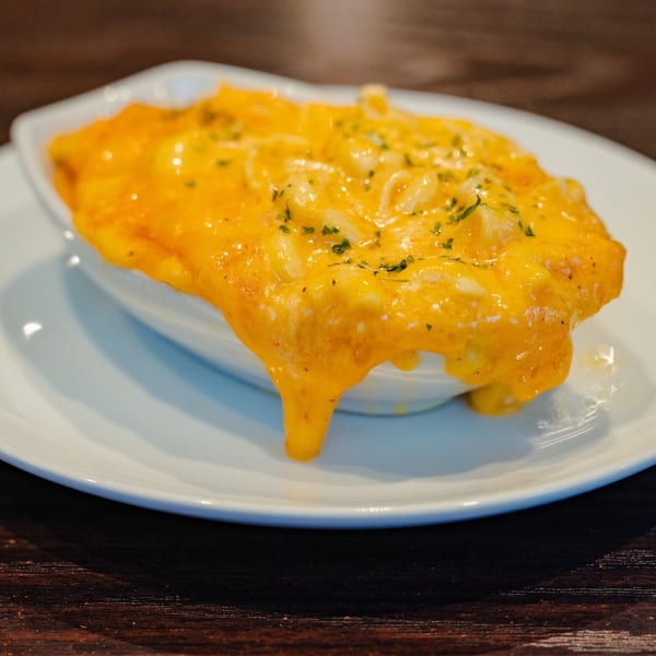 Creamy mac and cheese with melted orange cheese and green herbs in a white bowl on a dark wooden table.