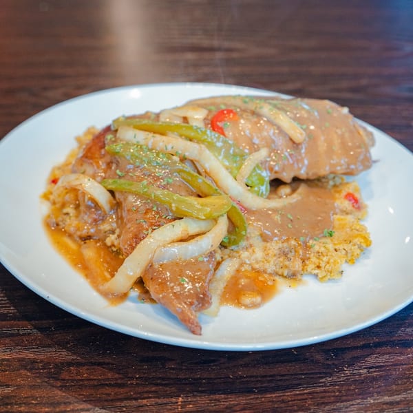 Steaming smothered pork chops with gravy, onions, and peppers over rice on a white plate.
