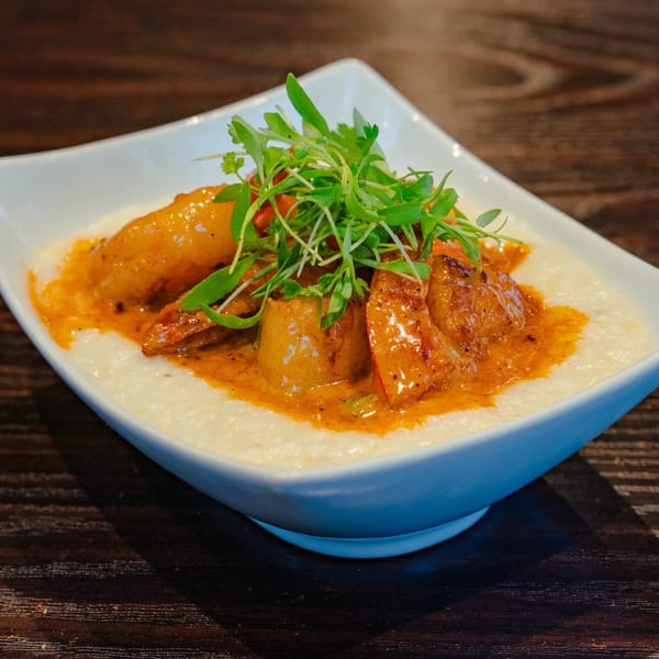 Shrimp and grits dish with a rich sauce and fresh greens in a white bowl.