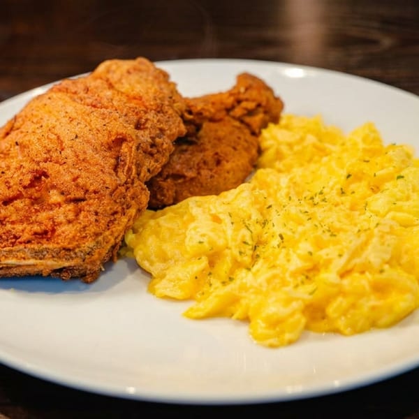 Crispy fried chicken and fluffy scrambled eggs with herbs on a white plate.