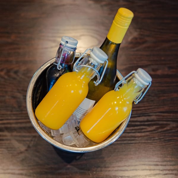 An ice bucket with a wine bottle and three smaller bottles of orange juice on a wooden table.