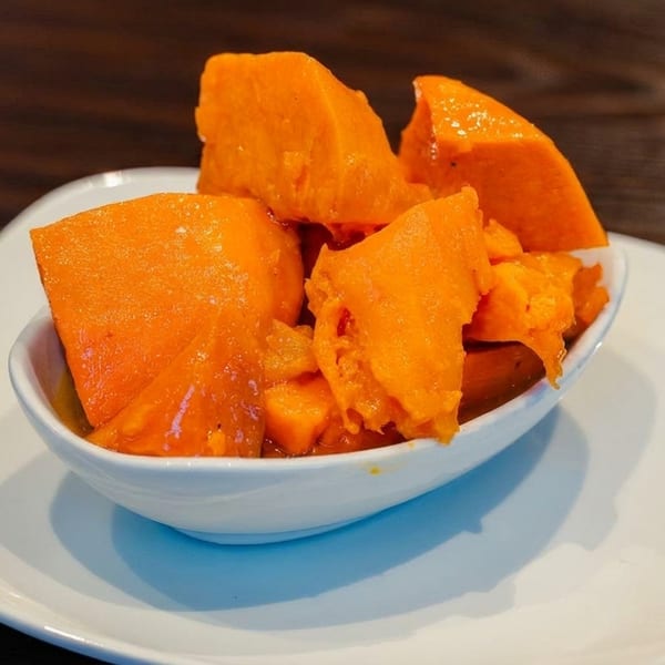 A white bowl filled with bright orange sweet potato chunks, served on a white plate.