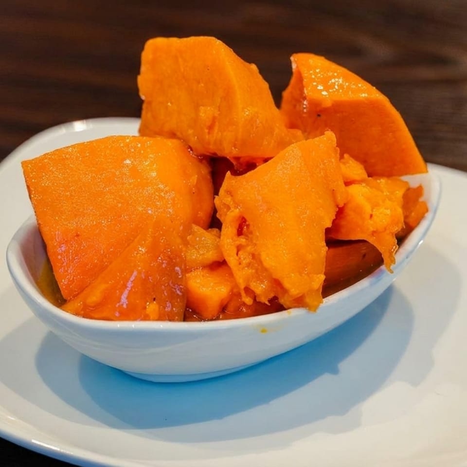 A white bowl filled with bright orange sweet potato chunks, served on a white plate.