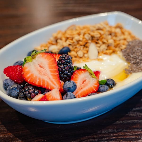 A white bowl filled with yogurt, granola, fresh berries, and chia seeds on a wooden table.