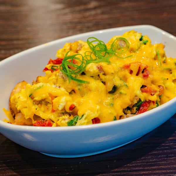 A white bowl filled with cheesy scrambled eggs, red peppers, and green onions on a wooden table.