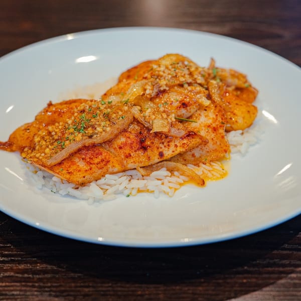 Spicy fish fillets with onions and herbs, served over white rice on a white plate.