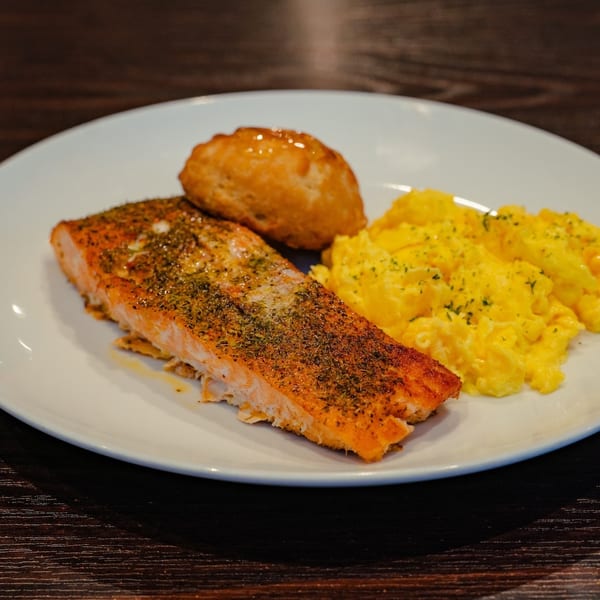 Seasoned salmon fillet, scrambled eggs, and a golden biscuit on a white plate.